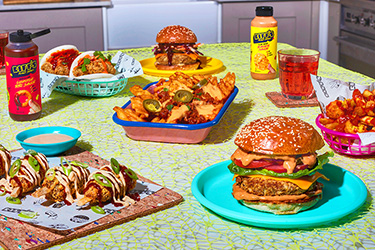 Lifestyle dinner table shot of Biff's Plant Shack wingz, burgers, sides and sauces available in Waitrose